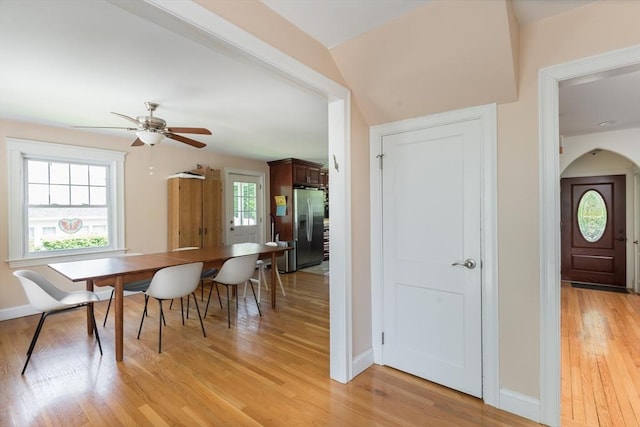dining space featuring light wood-style flooring, arched walkways, ceiling fan, and baseboards