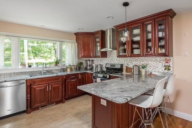 kitchen featuring appliances with stainless steel finishes, wall chimney exhaust hood, a sink, a peninsula, and a breakfast bar area