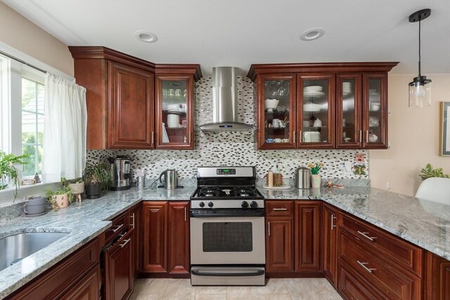 kitchen with stainless steel gas range, wall chimney exhaust hood, decorative backsplash, light stone counters, and pendant lighting