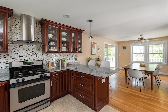 kitchen with stainless steel gas range, wall chimney range hood, backsplash, light wood-style flooring, and a peninsula