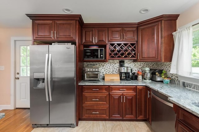 kitchen featuring stainless steel appliances, light stone countertops, decorative backsplash, and light wood-style floors