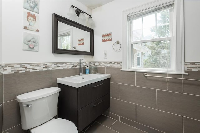 half bath featuring tile walls, toilet, healthy amount of natural light, tile patterned floors, and a wainscoted wall