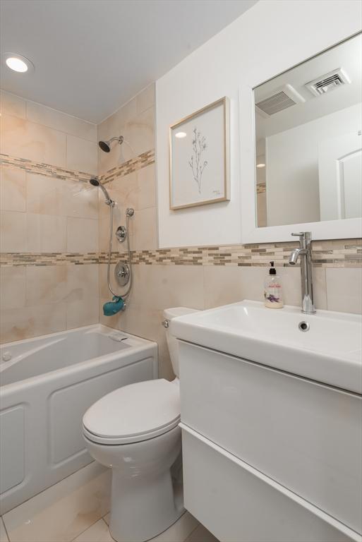 bathroom with toilet, tile walls, shower / washtub combination, vanity, and tasteful backsplash