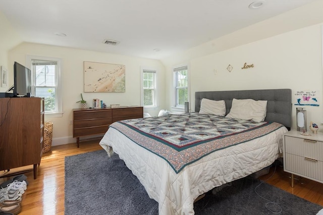 bedroom with wood finished floors, multiple windows, vaulted ceiling, and baseboards