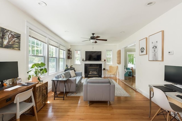 living area with a desk, a glass covered fireplace, a ceiling fan, light wood finished floors, and recessed lighting