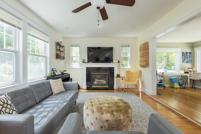 living room featuring plenty of natural light, wood finished floors, a tiled fireplace, and a ceiling fan