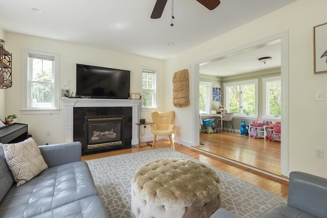 living area featuring wood finished floors, a fireplace with flush hearth, ceiling fan, and baseboards