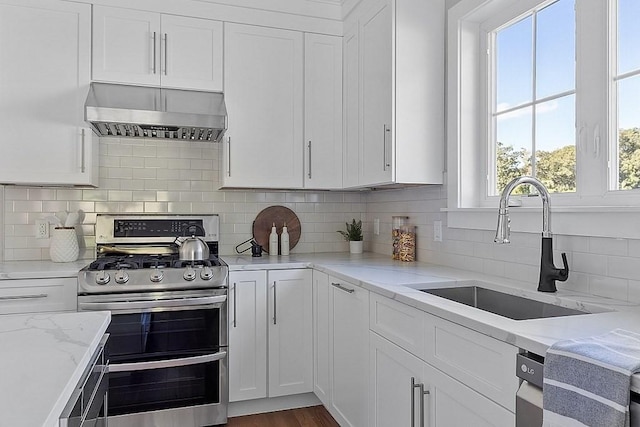 kitchen featuring sink, double oven range, ventilation hood, white cabinets, and decorative backsplash