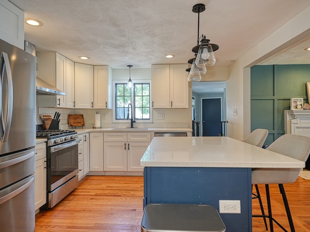 kitchen with sink, a kitchen breakfast bar, stainless steel appliances, pendant lighting, and light hardwood / wood-style flooring