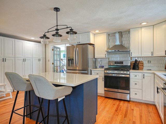 kitchen with wall chimney range hood, light hardwood / wood-style flooring, stainless steel appliances, backsplash, and white cabinetry