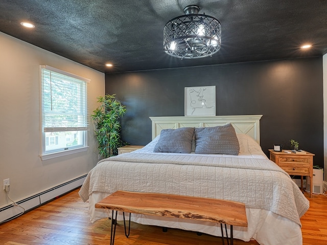 bedroom with a baseboard radiator, light hardwood / wood-style flooring, and a textured ceiling