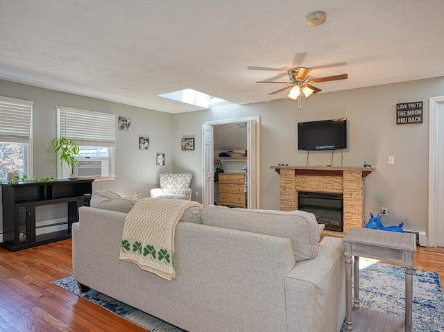 living room with a stone fireplace, cooling unit, wood-type flooring, a skylight, and ceiling fan