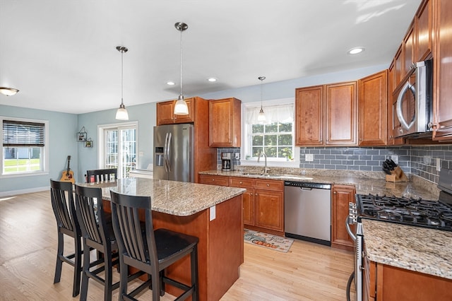 kitchen featuring a center island, light wood-type flooring, light stone countertops, stainless steel appliances, and a breakfast bar