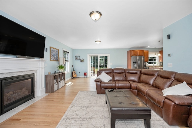 living room with a healthy amount of sunlight, a high end fireplace, and light hardwood / wood-style floors