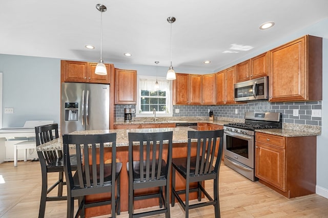 kitchen featuring light stone countertops, pendant lighting, appliances with stainless steel finishes, light hardwood / wood-style floors, and a kitchen bar