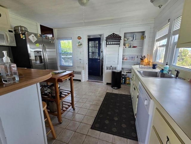 kitchen featuring radiator, white appliances, sink, light tile patterned floors, and built in features