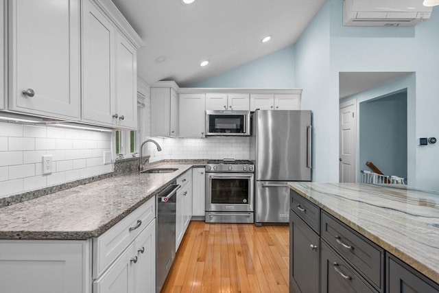 kitchen with stainless steel appliances, a sink, a wall mounted air conditioner, white cabinets, and vaulted ceiling