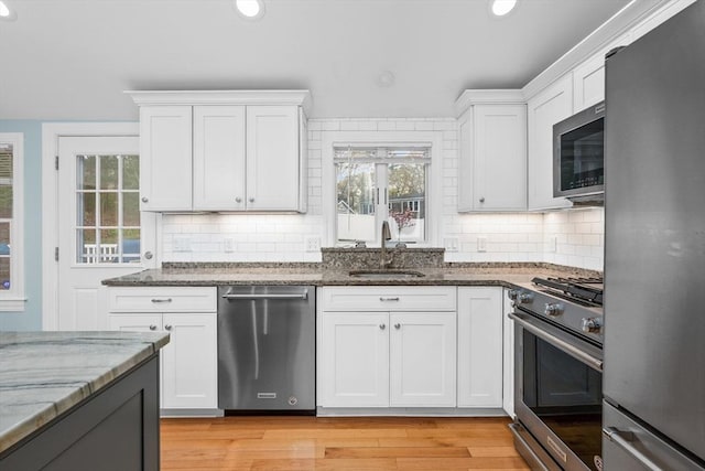 kitchen with appliances with stainless steel finishes, a sink, stone counters, white cabinetry, and recessed lighting
