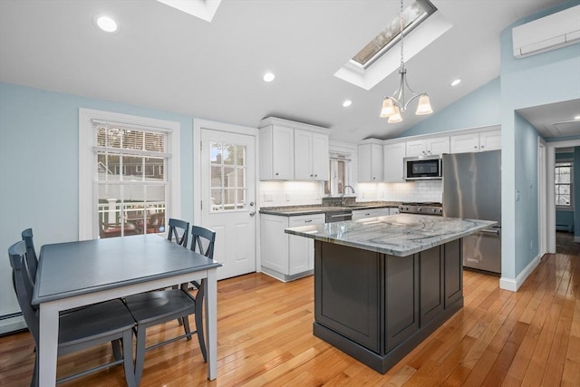 kitchen featuring stainless steel appliances, an AC wall unit, a skylight, white cabinets, and a kitchen island
