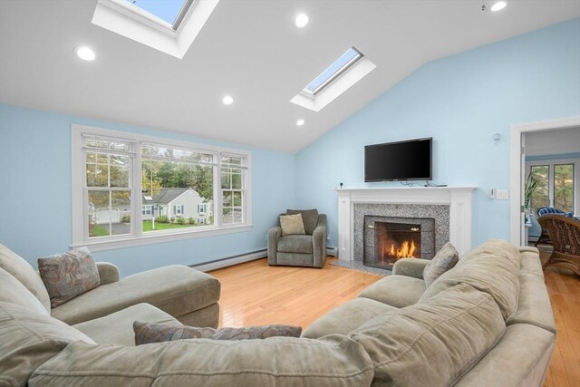 living room with a skylight, a baseboard heating unit, vaulted ceiling, wood finished floors, and a warm lit fireplace
