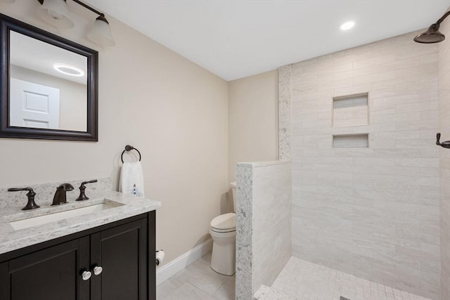 bathroom with toilet, tiled shower, vanity, baseboards, and recessed lighting