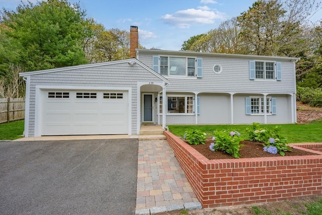 view of front of property featuring a chimney, driveway, an attached garage, and fence
