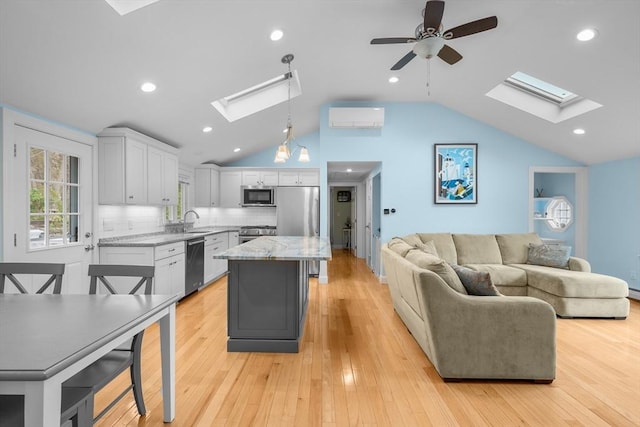 kitchen with a skylight, stainless steel appliances, a sink, vaulted ceiling, and white cabinetry