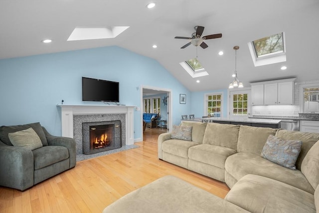 living room with a skylight, ceiling fan, light wood-type flooring, lofted ceiling, and a warm lit fireplace