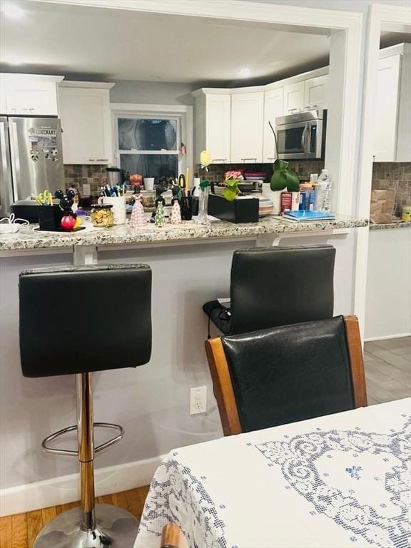 kitchen featuring white cabinetry, light stone counters, backsplash, wood-type flooring, and appliances with stainless steel finishes