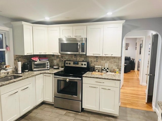 kitchen with sink, backsplash, appliances with stainless steel finishes, white cabinets, and light wood-type flooring