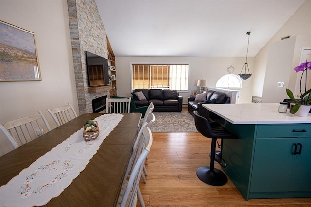 dining room with light wood finished floors, a fireplace, and high vaulted ceiling