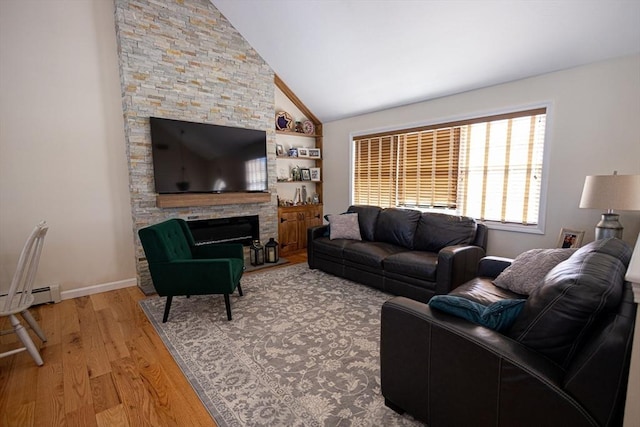 living area featuring baseboards, lofted ceiling, a stone fireplace, and light wood finished floors