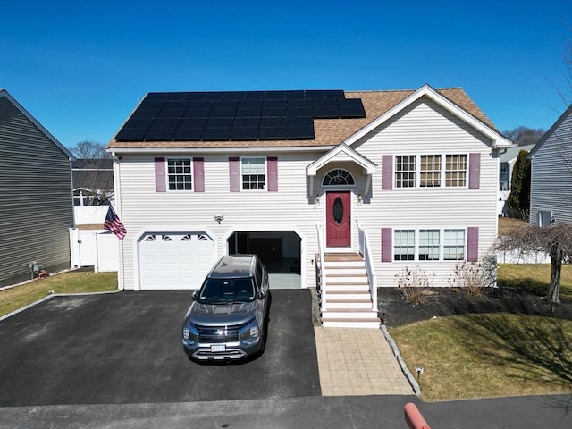 raised ranch with solar panels, a garage, driveway, and roof with shingles