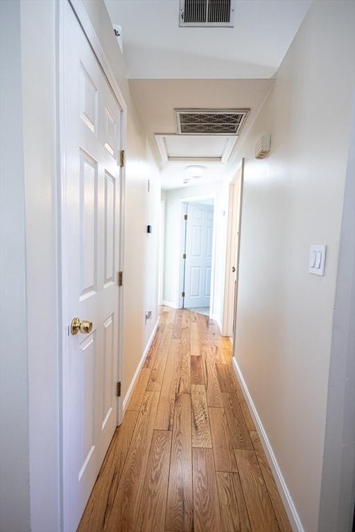 corridor featuring attic access, light wood-style flooring, baseboards, and visible vents