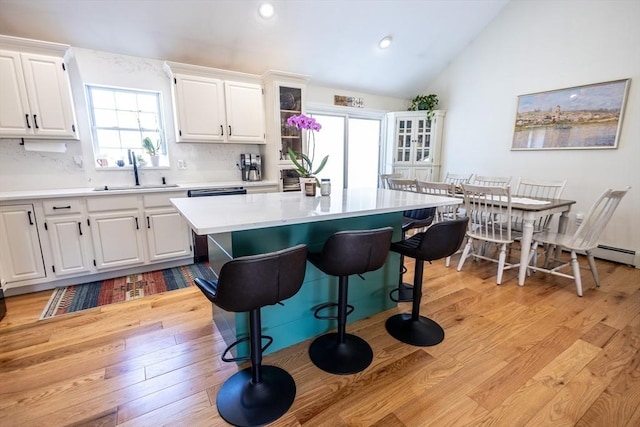 kitchen with a breakfast bar area, vaulted ceiling, light wood-style floors, white cabinetry, and a sink