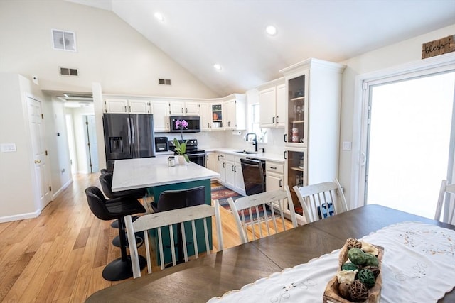 dining space featuring light wood-style flooring, visible vents, and high vaulted ceiling