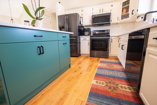 kitchen with light wood finished floors, appliances with stainless steel finishes, white cabinets, light countertops, and glass insert cabinets