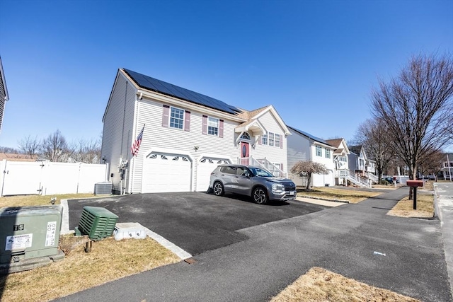 view of front of house with central air condition unit, driveway, roof mounted solar panels, a residential view, and an attached garage