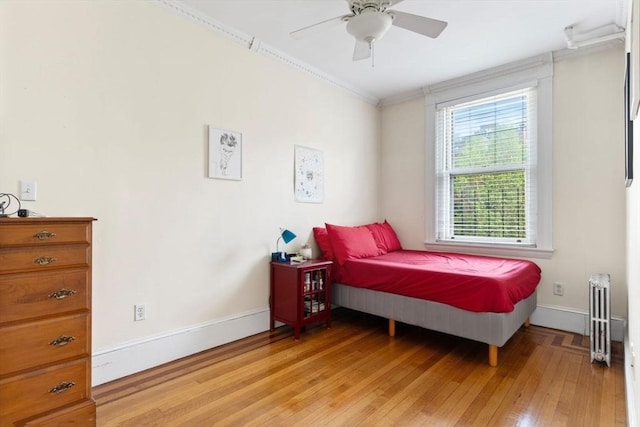 bedroom with radiator, light wood-type flooring, crown molding, baseboards, and ceiling fan