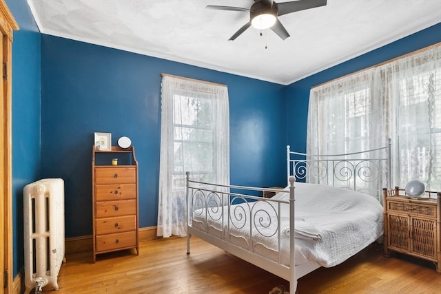 bedroom with wood-type flooring, ceiling fan, and radiator heating unit