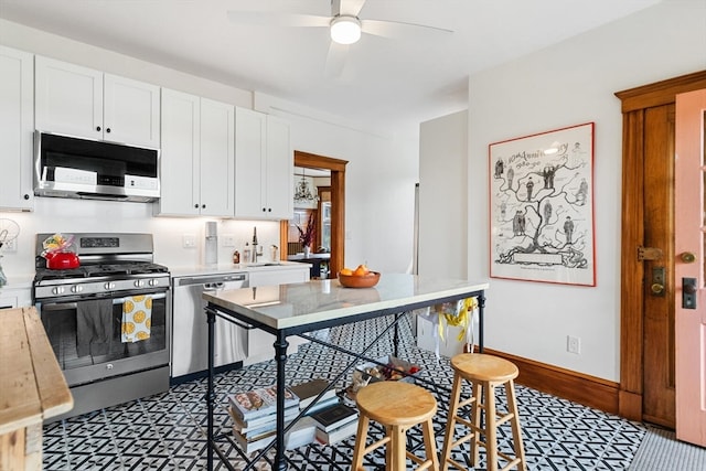 kitchen with appliances with stainless steel finishes, a breakfast bar area, ceiling fan, and white cabinets