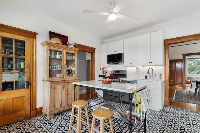 kitchen with a breakfast bar, sink, white cabinetry, stainless steel appliances, and ceiling fan