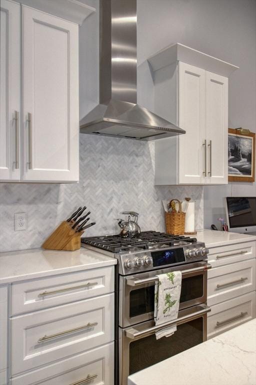 kitchen with light stone counters, double oven range, decorative backsplash, white cabinetry, and wall chimney exhaust hood