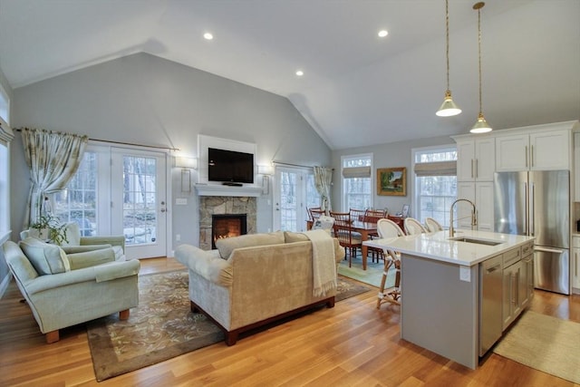 living area with a stone fireplace, recessed lighting, high vaulted ceiling, and light wood-style floors