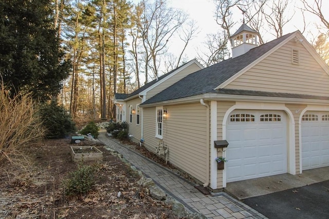 view of side of property featuring a garage, roof with shingles, and a vegetable garden