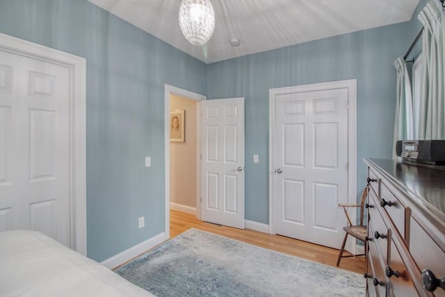 bedroom featuring an inviting chandelier, light wood-type flooring, and baseboards