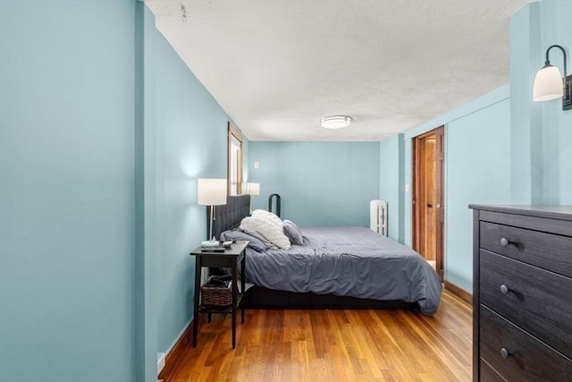 127 Highland Ave, Watertown, MA 02472 - bedroom featuring radiator heating unit, light wood-style floors, a textured ceiling, and baseboards