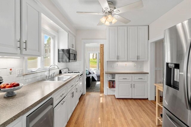 127 Highland Ave, Watertown, MA 02472 - kitchen featuring appliances with stainless steel finishes, a sink, white cabinetry, backsplash, and light wood-type flooring