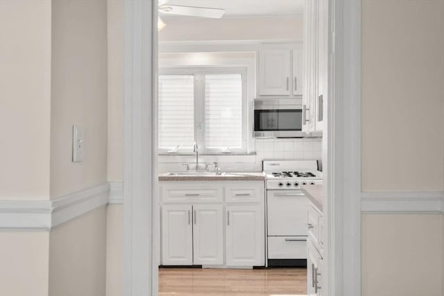 127 Highland Ave, Watertown, MA 02472 - kitchen with white gas stove, a sink, stainless steel microwave, white cabinets, and light countertops