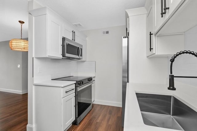 kitchen with pendant lighting, dark hardwood / wood-style flooring, sink, white cabinets, and stainless steel appliances